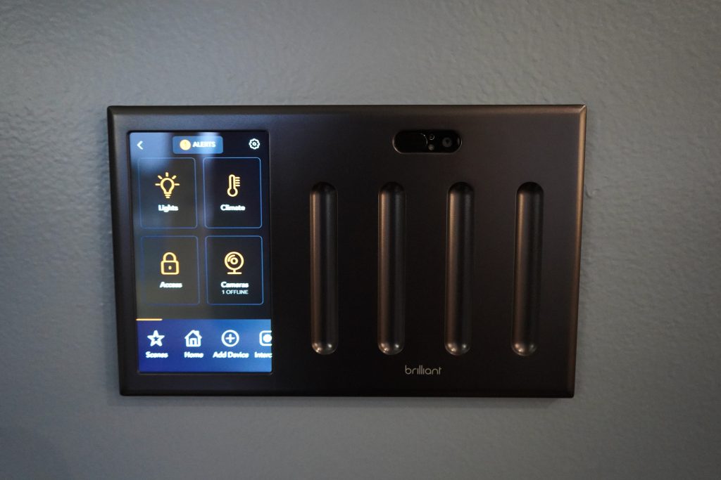 Brilliant wall-mounted smart-home touchscreen beside light switches.